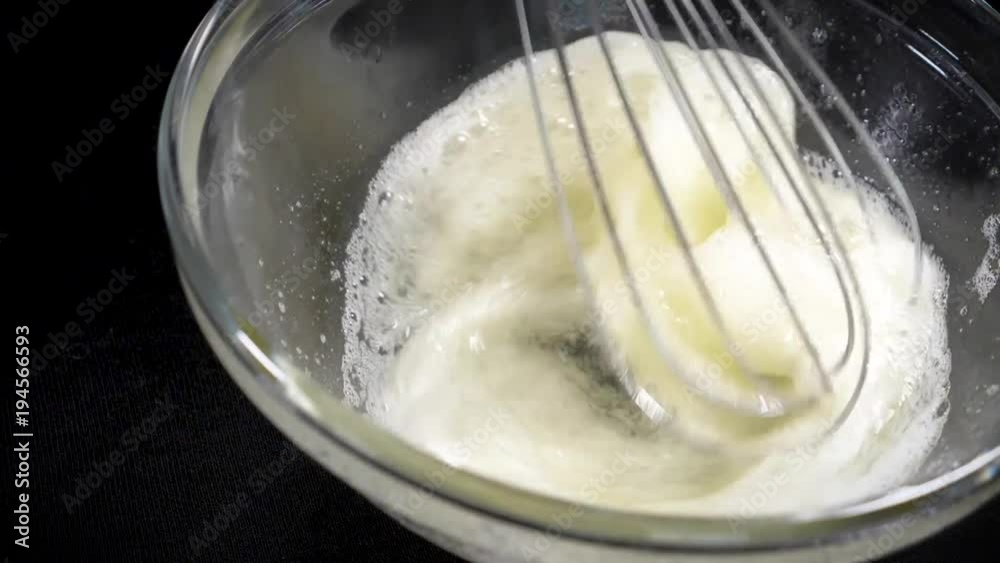 The cook brews the eggs. Whisk egg white. Black background. Slow motions The cook brews the eggs. Whisk egg white. Black background. Slow motions