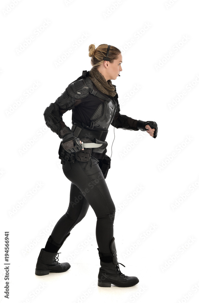 full length portrait of female  soldier wearing black  tactical armour, holding a remote knife, isolated on white studio background.