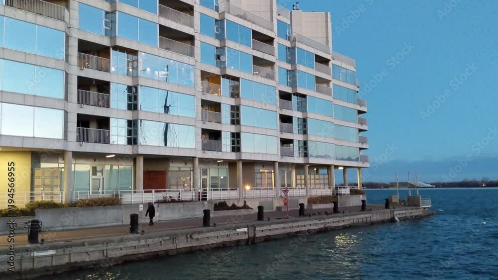 lone walker on the shore of lake Ontario in Toronto Harbourfront at dusk with multiple sky reflections on windows in the background lone walker on the shore of lake Ontario in Toronto Harbourfront at dusk with multiple sky reflections on windows in the background
