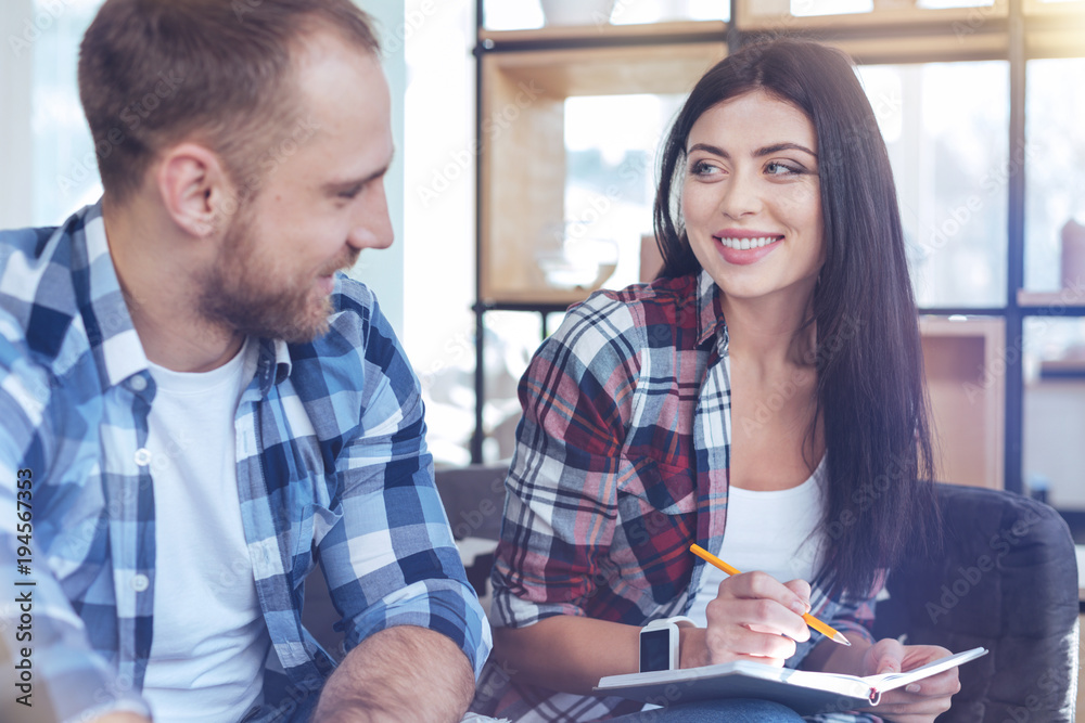 Obraz premium Be positive. Charming woman keeping smile on her face and looking at her best friend while making notes