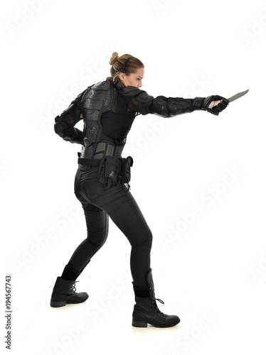 full length portrait of female soldier wearing black tactical armour, holding a remote knife, isolated on white studio background.