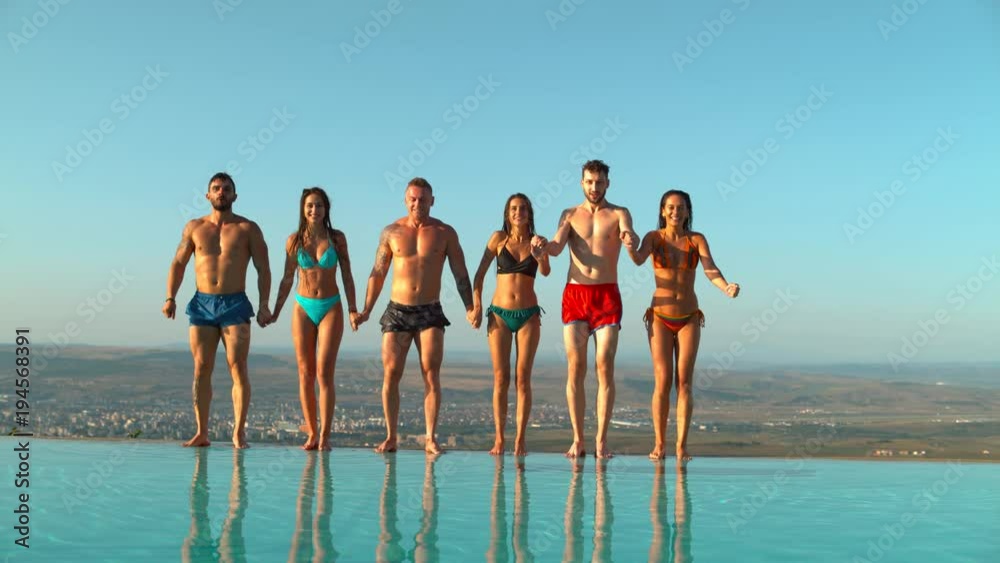 Friends holding hands and jumping in water Friends holding hands and jumping in water