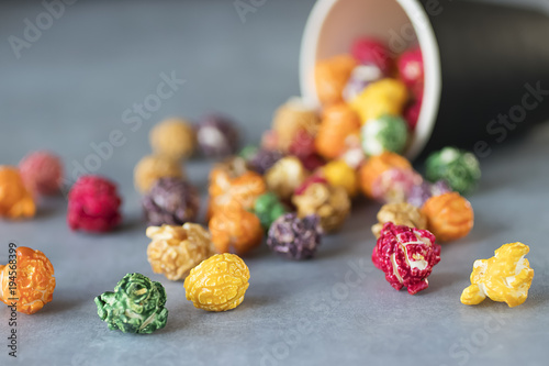 Multicolored popcorn and black paper cup on gray background.