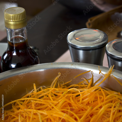 Shredded carrots in a professional large steel pan. Sauce and spices at the background photo