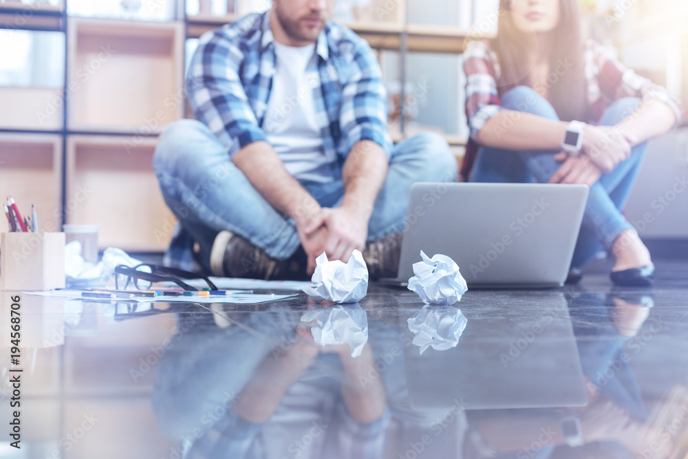 Obraz premium Casual lifestyle. Attentive man bowing head while looking at laptop and sitting on the floor near his colleague