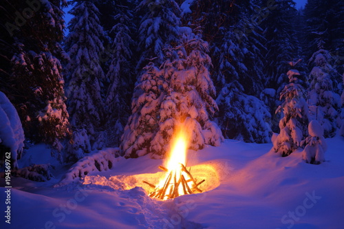 Bonfire in the winter forest illuminates the snow.