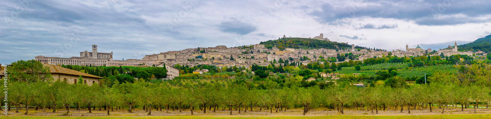 Panoramic view of the ancient town of Assisi with dramatic cloudscape and golden harvest fields, Umbria, Italy