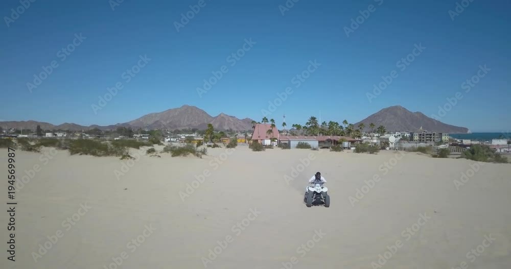 Aerial view of ATV 4-wheeler going across the sand in an exotic setting with palm trees, mountains and sea. Aerial view of ATV 4-wheeler going across the sand in an exotic setting with palm trees, mountains and sea.