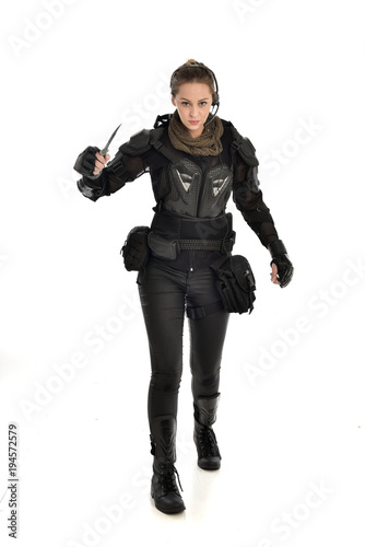 full length portrait of female  soldier wearing black  tactical armour, holding a remote knife, isolated on white studio background. © faestock