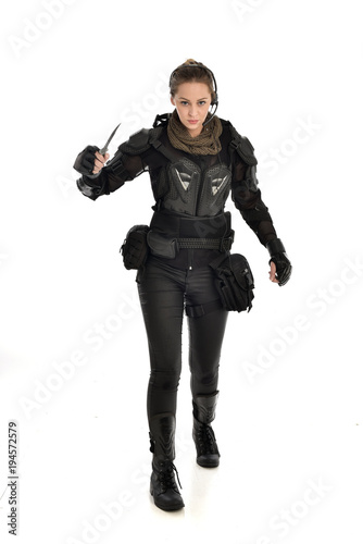 full length portrait of female soldier wearing black tactical armour, holding a remote knife, isolated on white studio background.