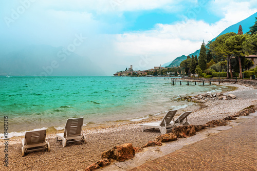Liegestühle am Gardasee Badestrand Malcesine, türkisblaues Wasser und Blick zur Burg