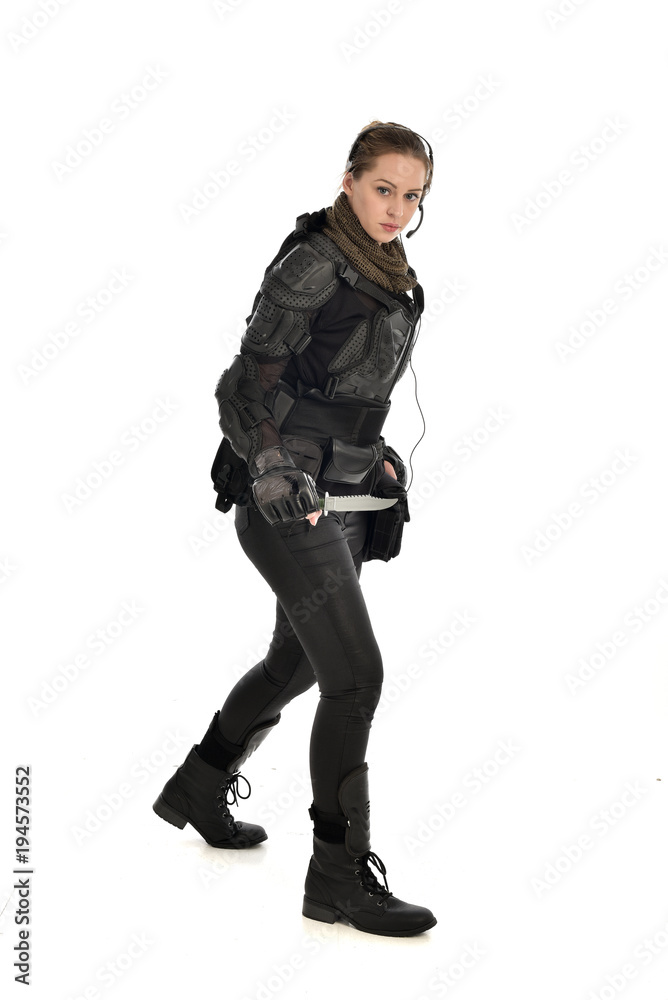 full length portrait of female  soldier wearing black  tactical armour, holding a remote knife, isolated on white studio background.