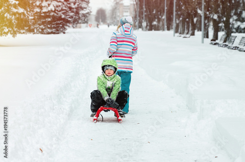 A woman is carrying a child on a sled. Mom walks with her son on the snow trail. Cheerful winter vacation. Winter fun. Baby on the sleigh.