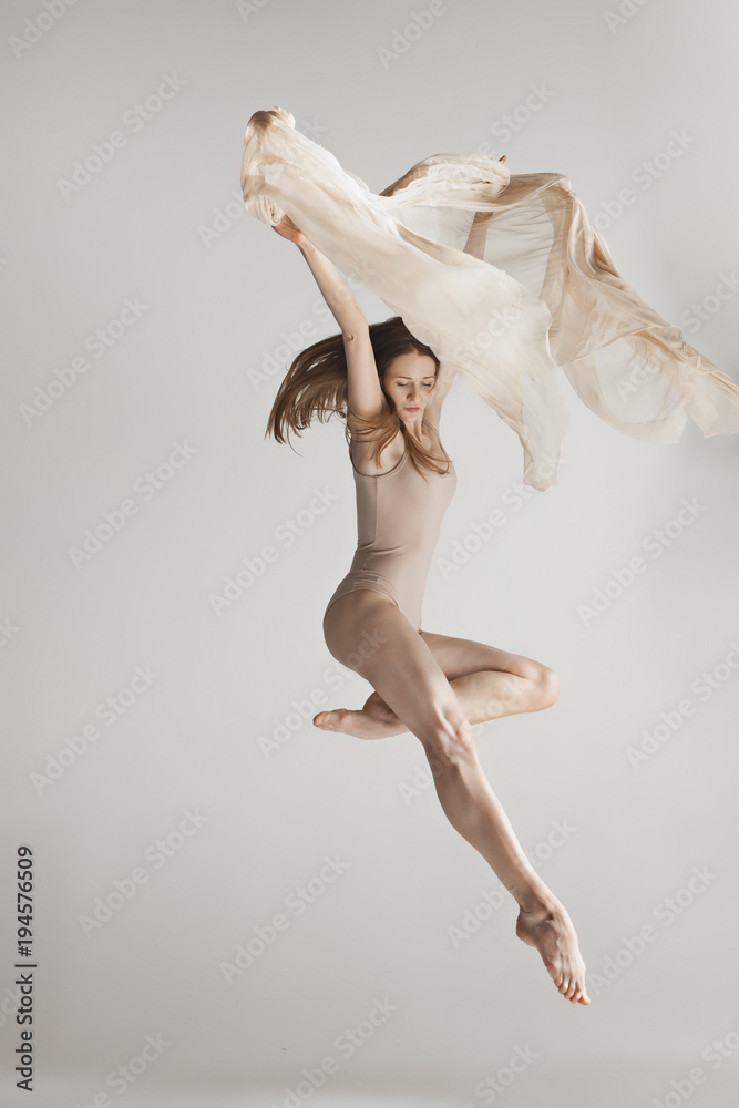 Young beautiful dancer in beige swimsuit dancing on gray background