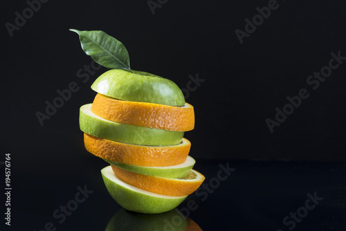 Slices of green apple with orange stacked in a pile on a black background.