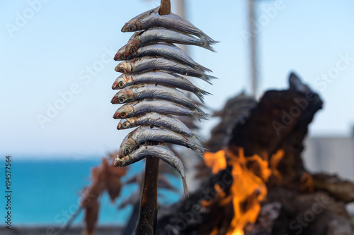an Holzkohle gegrillte Sardinen mit Flammen und glühender Kohle imHintergrund