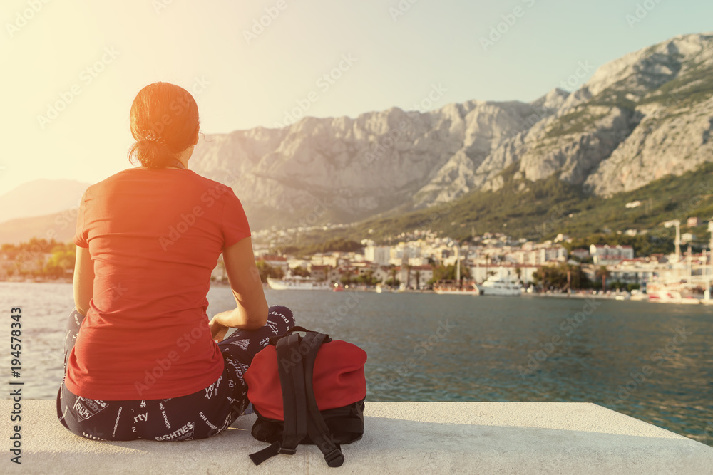 Fototapeta premium Girl sitting on a pier and watching the sunset.
