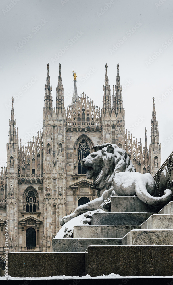 Fototapeta premium Falling snowflakes at ornate of lion on Piazza del Duomo in Milan, Lombardy, Italy. The Patron Saint of Milan, Madonnina, is visible above the Duomo Cathedral, with copy space