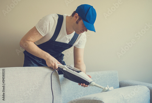 Man in uniform cleaning sofa with dry steam cleaner. Place for text.