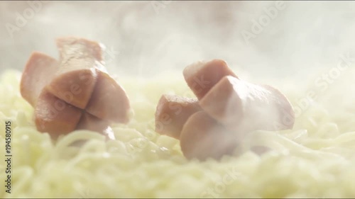 pieces of fried sausages fall on hot noodles with steam. slow motion photo