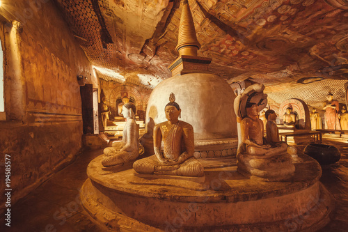 Dark interior of 1st century BC cave temple with sitting and meditating Gautama Buddha and painted ceiling