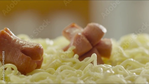 pieces of fried sausages fall on hot noodles with steam. slow motion photo