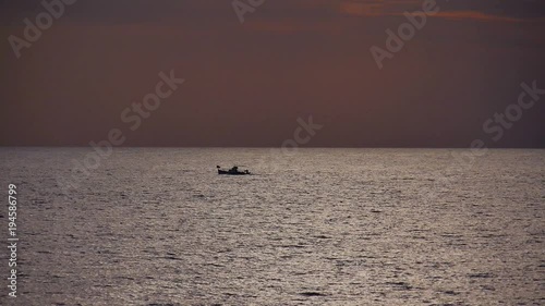 Long shot of fishing boat cruising across calm waters under dark sunset sky photo