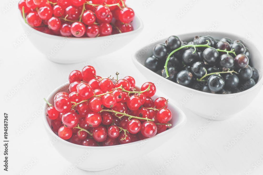 Ripe red and black currants in a white dish on a light background. Ripe red and black currants in a white dish on a light background.