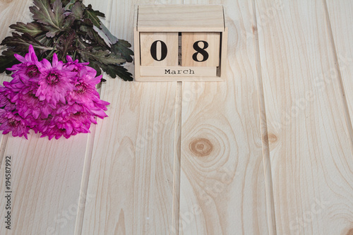 Wooden March 8 calendar, next to purple flowers on wooden table.