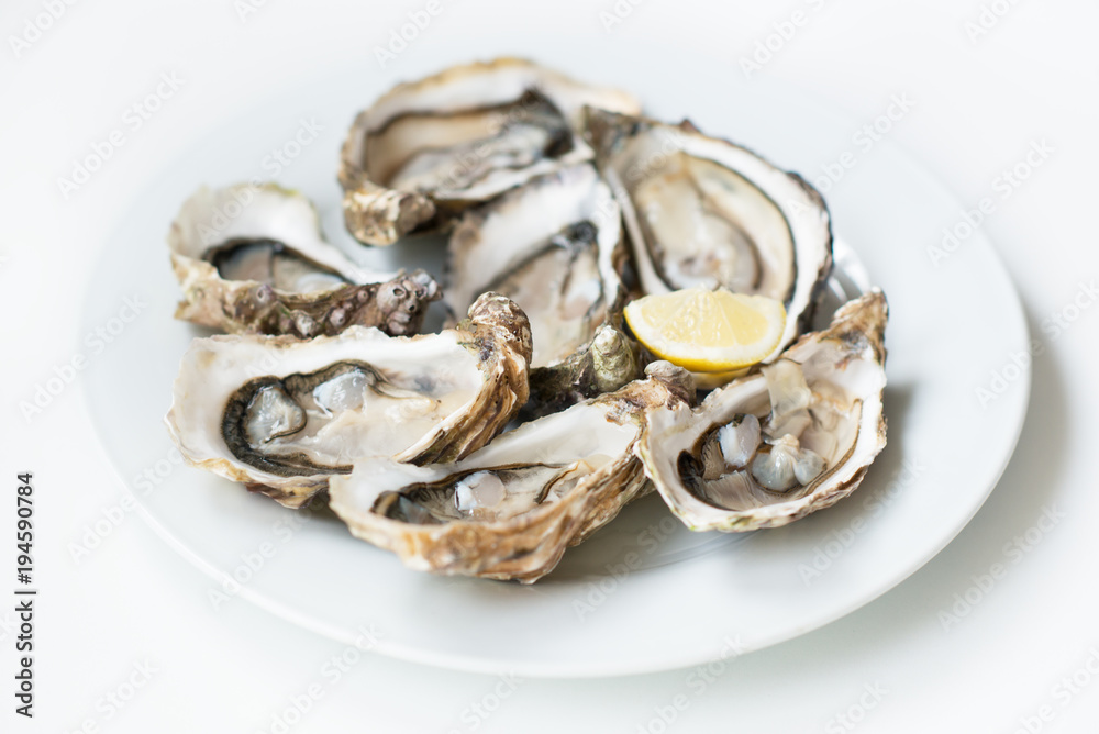 Oysters. Raw fresh oysters with lemon are on white round plate, image isolated, with soft focus. Restaurant delicacy. Oysters. Raw fresh oysters with lemon are on white round plate, image isolated, with soft focus. Restaurant delicacy.