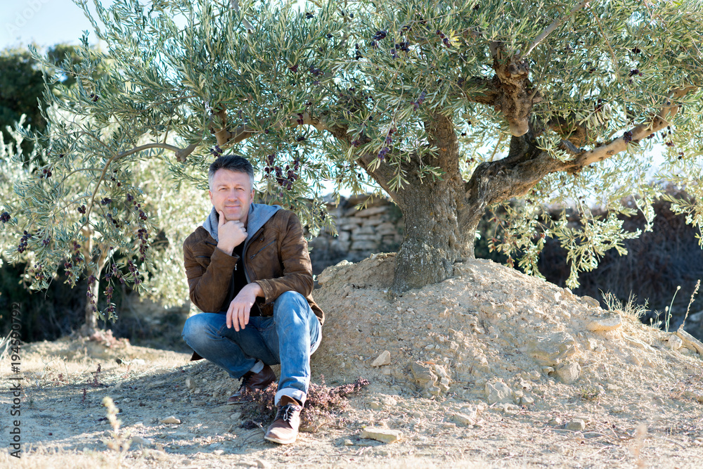 Handsome man posing in olive trees garden. Male portrain over mediterranean olive field ready for harvest. Confident mature man in spanish olive's grove with ripe fresh olives. Handsome man posing in olive trees garden. Male portrain over mediterranean olive field ready for harvest. Confident mature man in spanish olive's grove with ripe fresh olives.