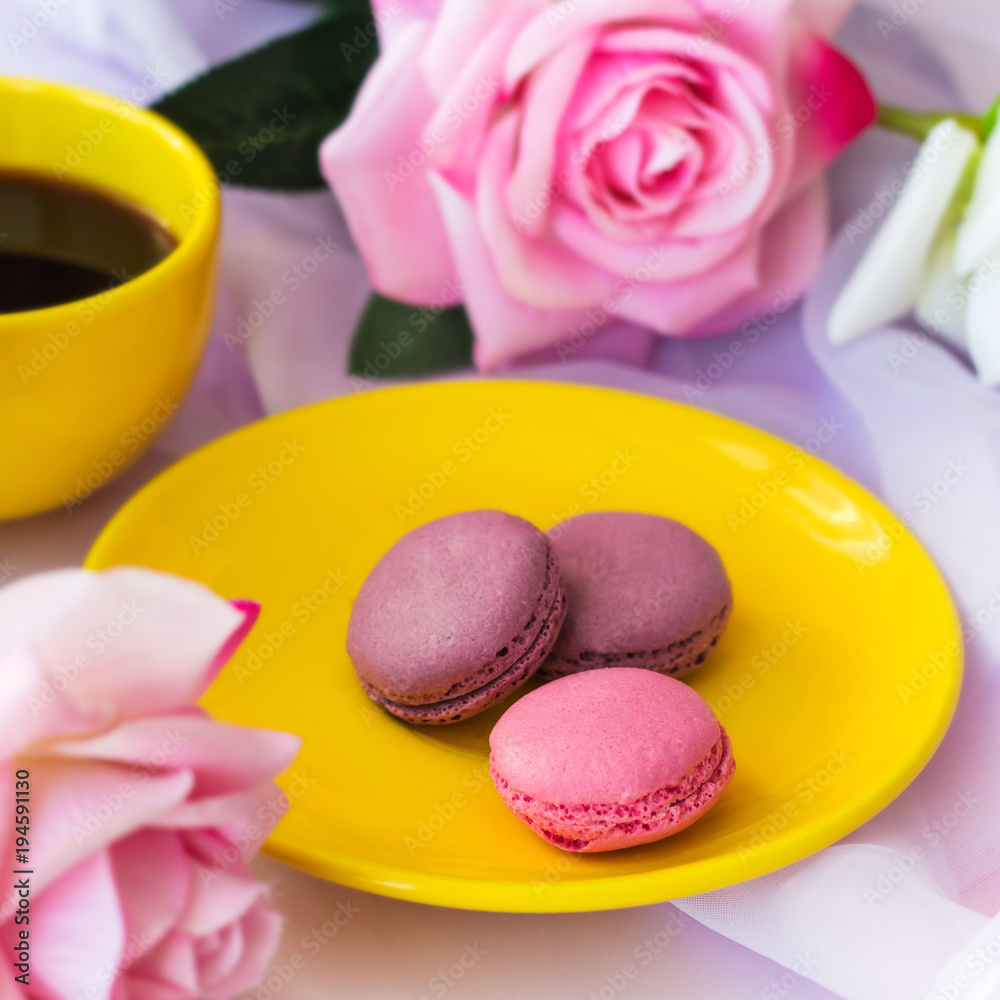 yellow hot drink cup and macaroons on a plate and blurred roses on a table yellow hot drink cup and macaroons on a plate and blurred roses on a table