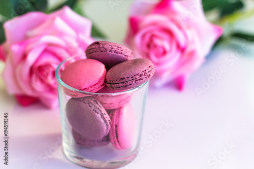Photography colored delicious macarons in a glass on the blurry background of pink roses