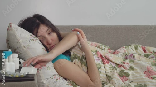 Young woman with a cold. Sits on a bed in a blanket. photo