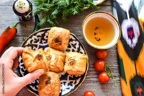 woman's hand hold samosa and delicious Uzbek pieces of samosas with cherry tomatoes, Chile on the plate with Uzbek ornament on a wooden background in rustic style for breakfast, uzbek utensils photo