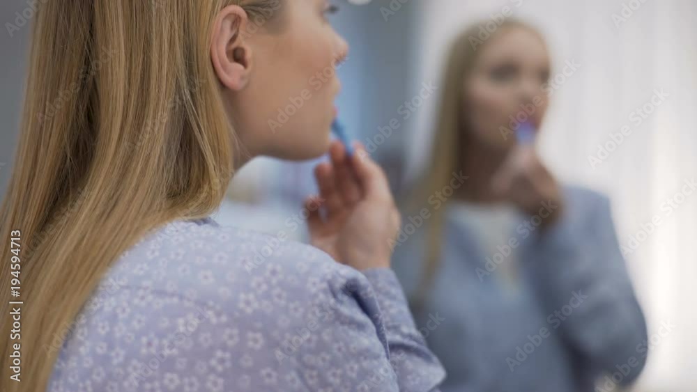 Young lady applying lipstick before date, altering appearance by make up