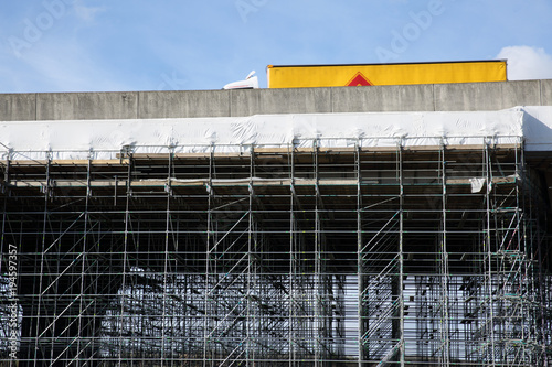 A lorry crosses a section of elevated motorway bridge that has a complex scaffolding structure underneath. Highway maintenance on a flyover with a scaffold support frame beneath.