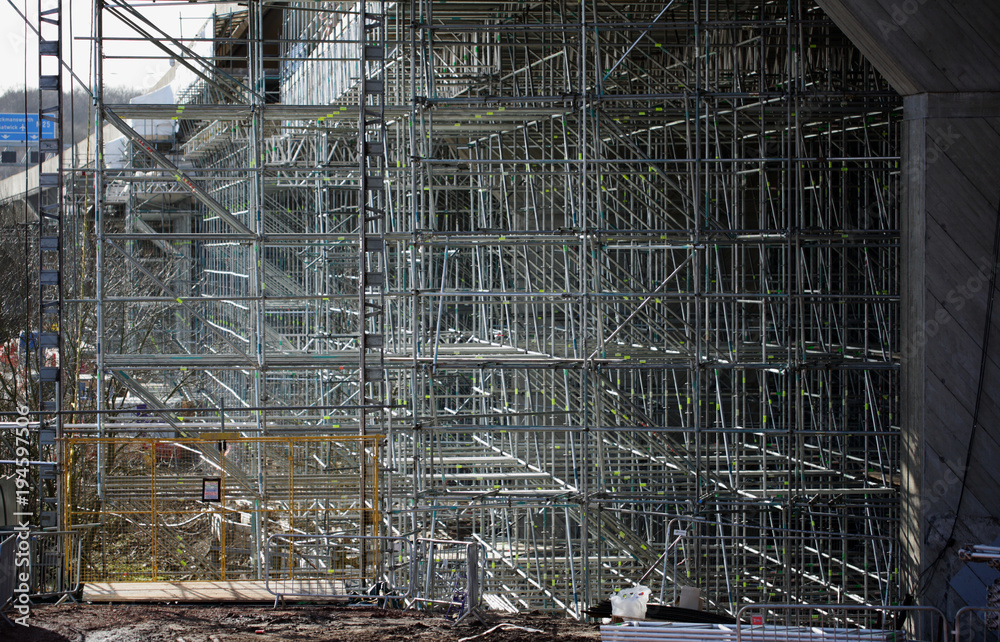 Complex steel scaffolding structure enabling repair and inspection of a motorway bridge. Highway maintenance of the underside of a long flyover. Steel scaffold bars form a 3D cube pattern frame.