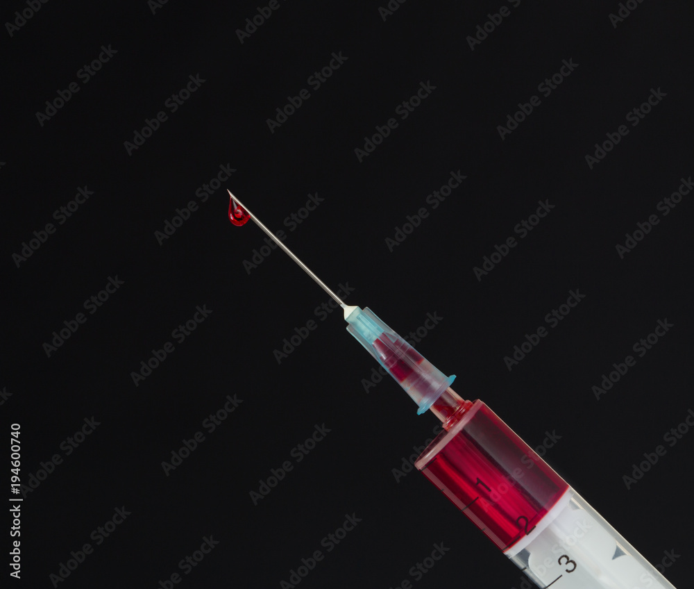 Syringe with a drop of blood on a needle on a black background