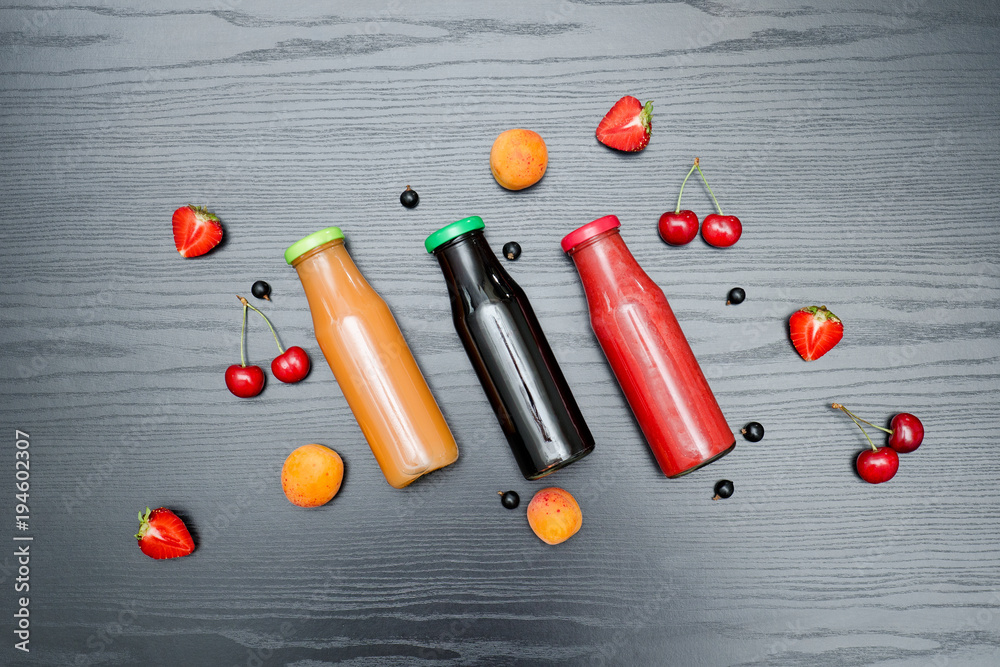 Three bottles of juice and fruits. Black wooden background. Food concept