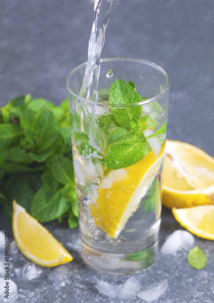 Glass of aced water with lemon and mint. Water drink pouring into glass Glass of aced water with lemon and mint. Water drink pouring into glass