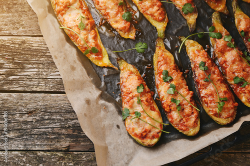 Baked stuffed zucchini with meat in a pan on wooden boards.