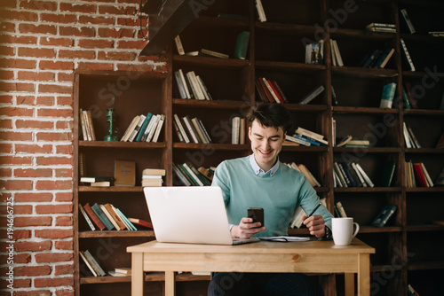 Young handsome guy is going to enter university and prepares for exams in different fields with the help of his laptop and books in the library. Student planning his lessons at the university.