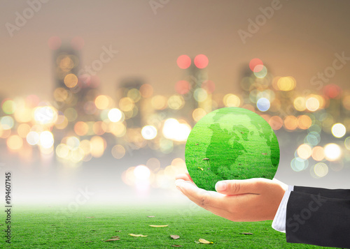 World environment day concept: Businessman hand holding earth globe of grass over blurred city background
