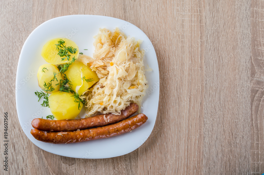 Roasted sausages with steamed cabbage (sauerkraut) and boiled potatoes in white plate. Roasted sausages with steamed cabbage (sauerkraut) and boiled potatoes in white plate.