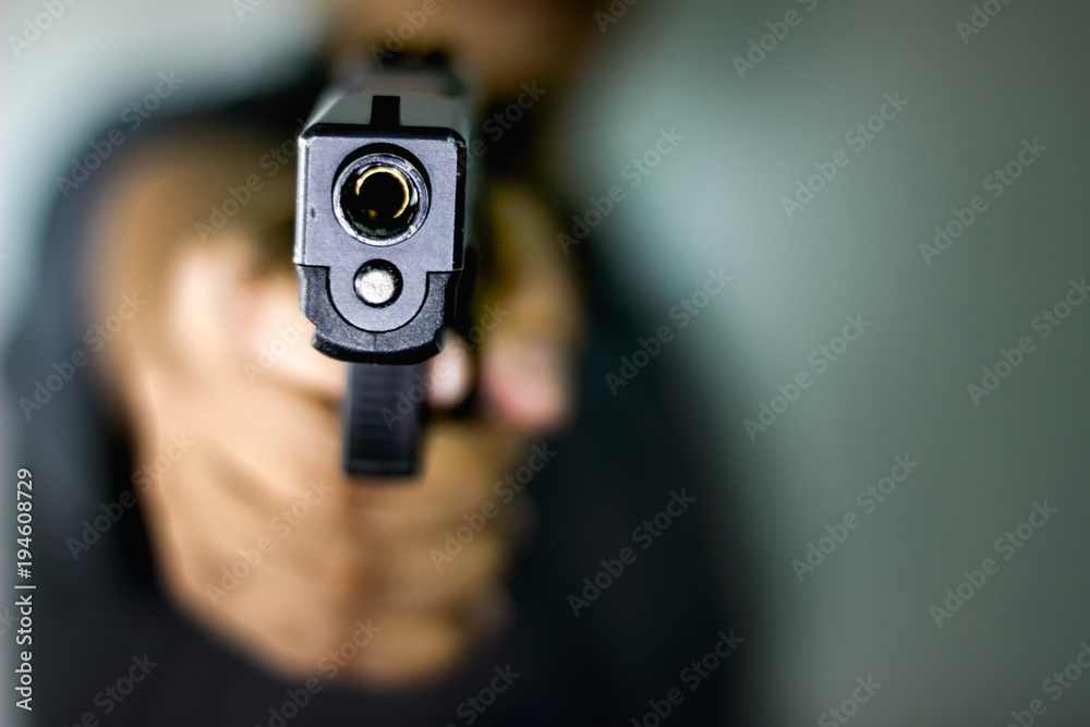 A man holding a gun pointing to a target demonstrates the violence of a gun with blurry background A man holding a gun pointing to a target demonstrates the violence of a gun with blurry background