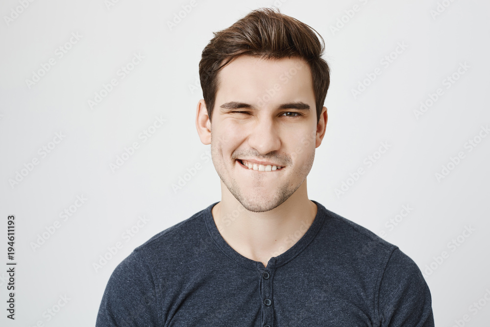 Attractive young macho winking and biting his lip, flirting with someone while standing over gray background. Hot boyfriend checks out girl who is looking at him in subway Attractive young macho winking and biting his lip, flirting with someone while standing over gray background. Hot boyfriend checks out girl who is looking at him in subway