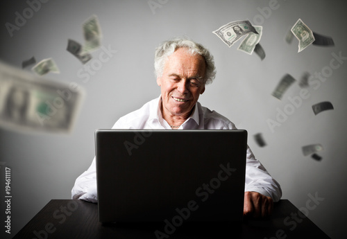 Old man using a laptop. Old man in white earns dollars on the internet.