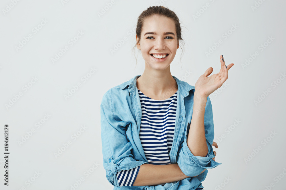 Laughter eases everyday problems. Charming woman in trendy outfit with bun hairstyle gesturing while talking to friend, standing with crossed hand over body and smiling broadly at camera Laughter eases everyday problems. Charming woman in trendy outfit with bun hairstyle gesturing while talking to friend, standing with crossed hand over body and smiling broadly at camera