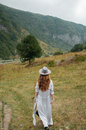 A girl in a hat walks near the mountains